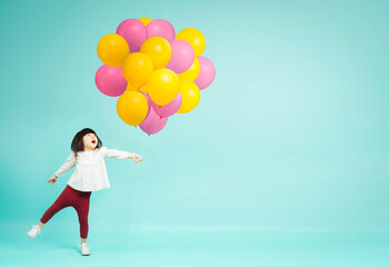 Fototapeta na wymiar Little girl holding helium balloons on plain background