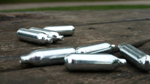 Closeup pile of chrome nitrous oxide dangerous gas drug cylinders on wooden bench dolly right on wooden park table