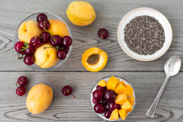 Healthy vegan breakfast of chia seed pudding topped with fresh apricots and cherries. More fruit and a vintage silver spoon in the wooden background. Rustic and dark aesthetic