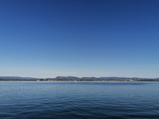 Beautiful calm day on the sea with clear blue sky and island with pine trees