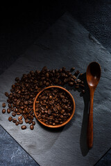 Freshly roasted coffee beans in a wooden bowl. A natural stone. Dark background. A scattering of coffee beans on a stone surface.