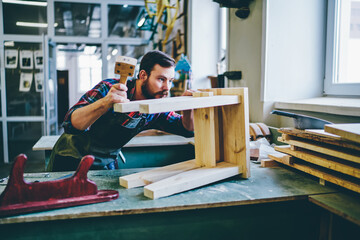 Self employed owner of restoration manufacture doing engineering with wood equipment, Caucasian man artisan in apron concentrated on improvement decorative handmade chair during working process