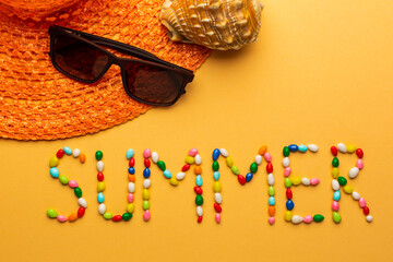 Word summer written with colorful candies on orange background with sun glasses and summer hat for seaside.