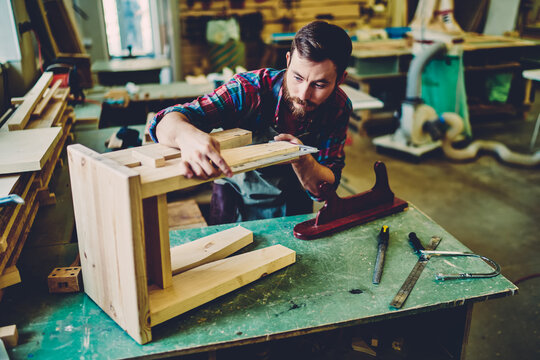 Caucasian craftsman making measurements for decorative chair during woodworking hobby in manufacturing restauration, bearded male worker concentrated on handmade equipment during engineering