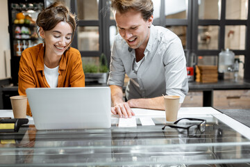 Two young managers or shop owners having some discussion working on a laptop at the counter of the shop or cafe. Small business management concept
