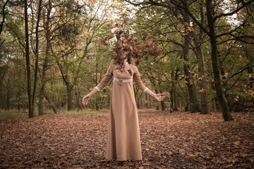 Woman in vintage dress in autumn forest throwing fall leaves in matching color palette