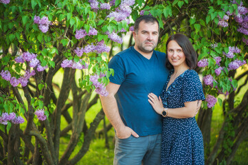 A beautiful couple, husband and wife are standing in a summer park near the lilac bushes, they are...