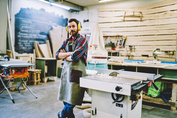 Half length portrait of self-employed woodman in work apron standing near lathe instument with...