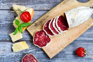 Italian  dried   artisan  pork salami,parmesan cheese ,peperoncino  and fresh basil on wooden background .Rustic  home made food