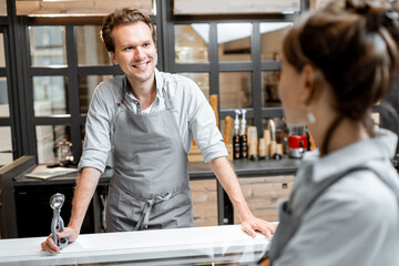 Portrait of a cheerful salesman in apron talking with a customer at the small shop or cafe. Concept of a small business and work in the field of services - obrazy, fototapety, plakaty