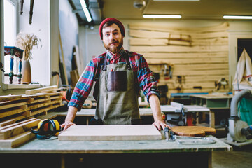 Half length portrait of prosperous male owner of craft store standing at working place with...
