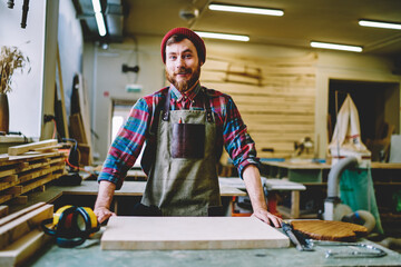 Cheerful caucasian male owner of restoration workshop looking at camera  satisfied with successful craft business,portrait of smiling handsome handyman in apron standing at working place  with tools - obrazy, fototapety, plakaty