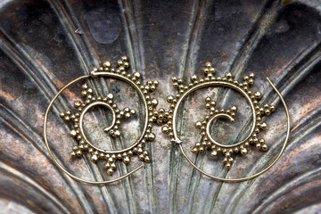 Brass metal spiral earrings on decorative silver shell background