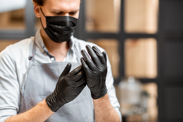 Seller in face mask and black gloves disinfecting hands while working in a grocery store or cafe....