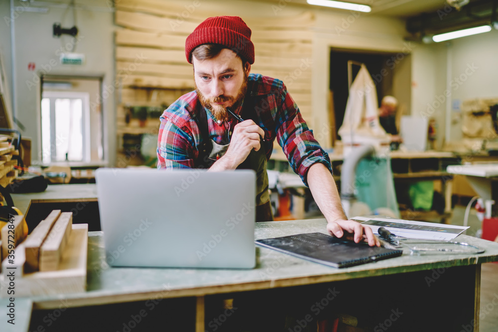 Poster serious bearded male master checking information from website while creating sketch and plannings fo