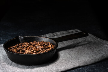 Freshly roasted coffee beans in a cast iron skillet. Linen napkin. A natural stone. Dark background.
