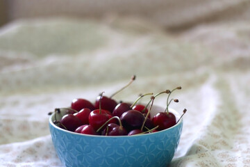 Bowl of fresh cherries on a bed with floral sheets. Selective focus.