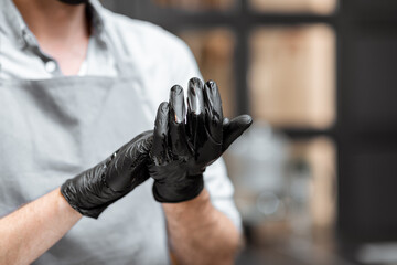 Seller in black gloves disinfecting hands while working in a grocery store or cafe, close-up view. Concept of a new rules for business during a pandemic