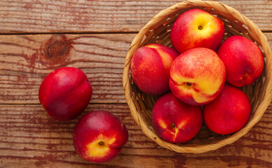 Nectarine. Ripe juicy organic nectarines (peaches) in a wicker basket. Whole fruit on a wooden table. Selective focus, top view, copy space