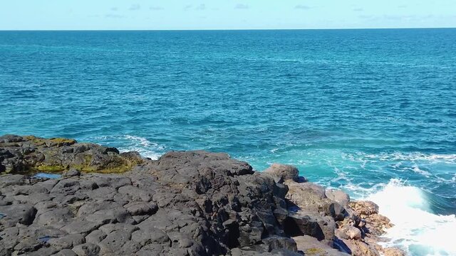 HD Hawaii Kauai slow motion static of ocean waves swirling and crashing against lava rock splashing in lower right quadrant with blue sky on ocean horizon