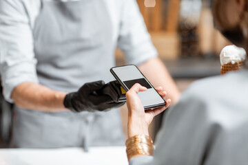 Seller in makes contactless payment for a client in the ice cream shop, close-up