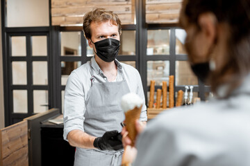 Salesman in protective mask selling ice cream for a young client in the shop. Concept of new social rules for business during a pandemic