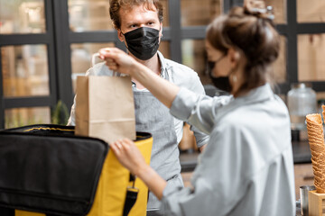 Female courier taking online order for delivery at the counter with salesperson in the small pastry shop or cafe. Concept of a take away food during pandemic