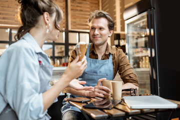Couple of a young cafe workers have some business conversation while sitting with coffee at the table of their cafe or pastry shop