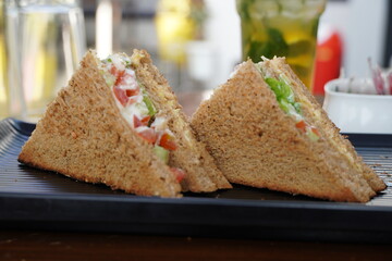 Two club sandwiches placed on a black plate at a restaurant. Close-up photo of a club sandwich. Sandwich with prosciutto, vegetables, lettuce and mayo on a fresh sliced rye bread on wooden background.