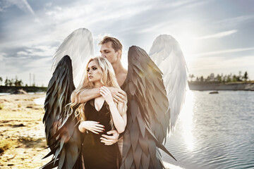 Romantic meeting of angels. Good and evil. A parken and a girl stand by the water at sunset.