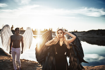 Romantic meeting of angels. Good and evil. A parken and a girl stand by the water at sunset.
