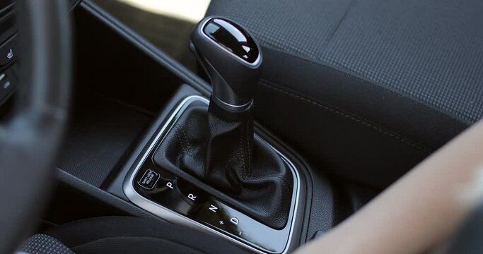 Female hand shifts gears. Automatic transmission, automatic gear shift, is moved from P (Park) to D (Drive). Side view.