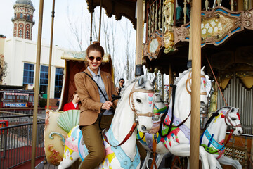 Attractive young woman having fun riding on carousel in amusement park