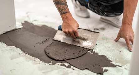 Handwerker gleicht einen Höhenunterschied im Estrich aus, in dem er mit der Glättkelle...