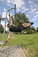 Young man in sports outfit doing workout in a city park at an outdoor gym