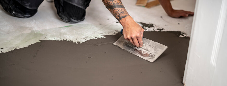 Bauarbeiter gleicht einen Höhenunterschied im Estrich aus, in dem er mit der Glättkelle schnelltrocknende standfeste Spachtelmasse aufzieht