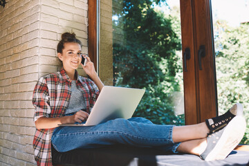 Portrait of young smiling hipster girl dressed in trendy outfit having mobile conversation on...