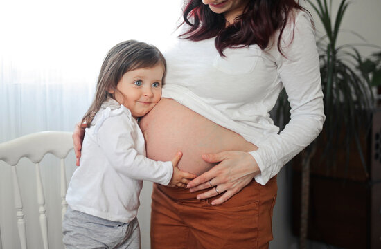 
little girl leaning on her mother's pregnant belly