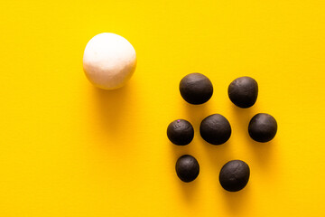 One big white ball and many black smaller plasticine balls in a group. Concepts of race and racism. White power and privilege. Area left for copyspace on yellow background
