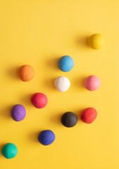 Many different colored plasticine balls on a yellow background. Colorful top down view, hand rolled childrens toys