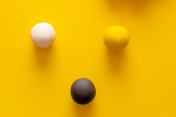 Black white and yellow balls standing together on a yellow background. Representing the main three human races, concepts of racism, social issues and separation