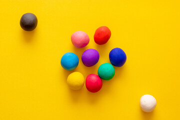 Black and white plasticine balls separated from many other colorful plastic balls on yellow background. Concepts of seclusion, difference, racism, unacceptance
