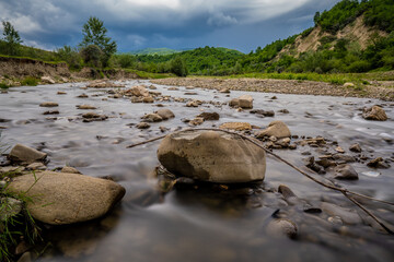 Long exposure low angle view with the flow of a mountain river that grows as the distant storm...