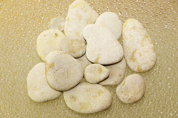 Gray smooth sea stones from the shore against the background of water drops. Backlight below. The color is golden.