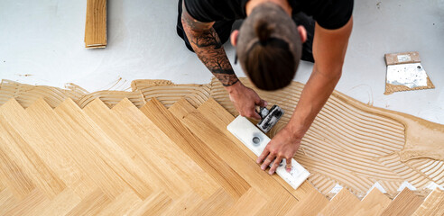 junger Parkettleger Meister schlägt die Dielen des Fischgrät Parketts mit dem Schlagholz und dem...