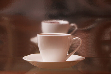 White cup with coffee on a glass table. Background - mirror 3D reflection.