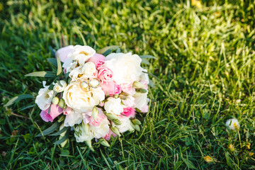 Wedding bouquet of the bride with wedding rings, lying on the green grass. Soft pink and beige tea roses are gathered in a romantic bouquet.