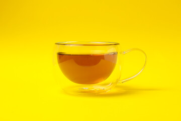Glass cup of chamomile tea on yellow background