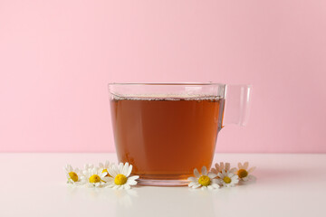 Cup of tea and chamomile on white table against pink background