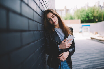 Half length portrait of attractive hipster girl enjoying free time outdoors strolling on spring day standing with smartphone on promotional background, beautiful young woman looking at camera